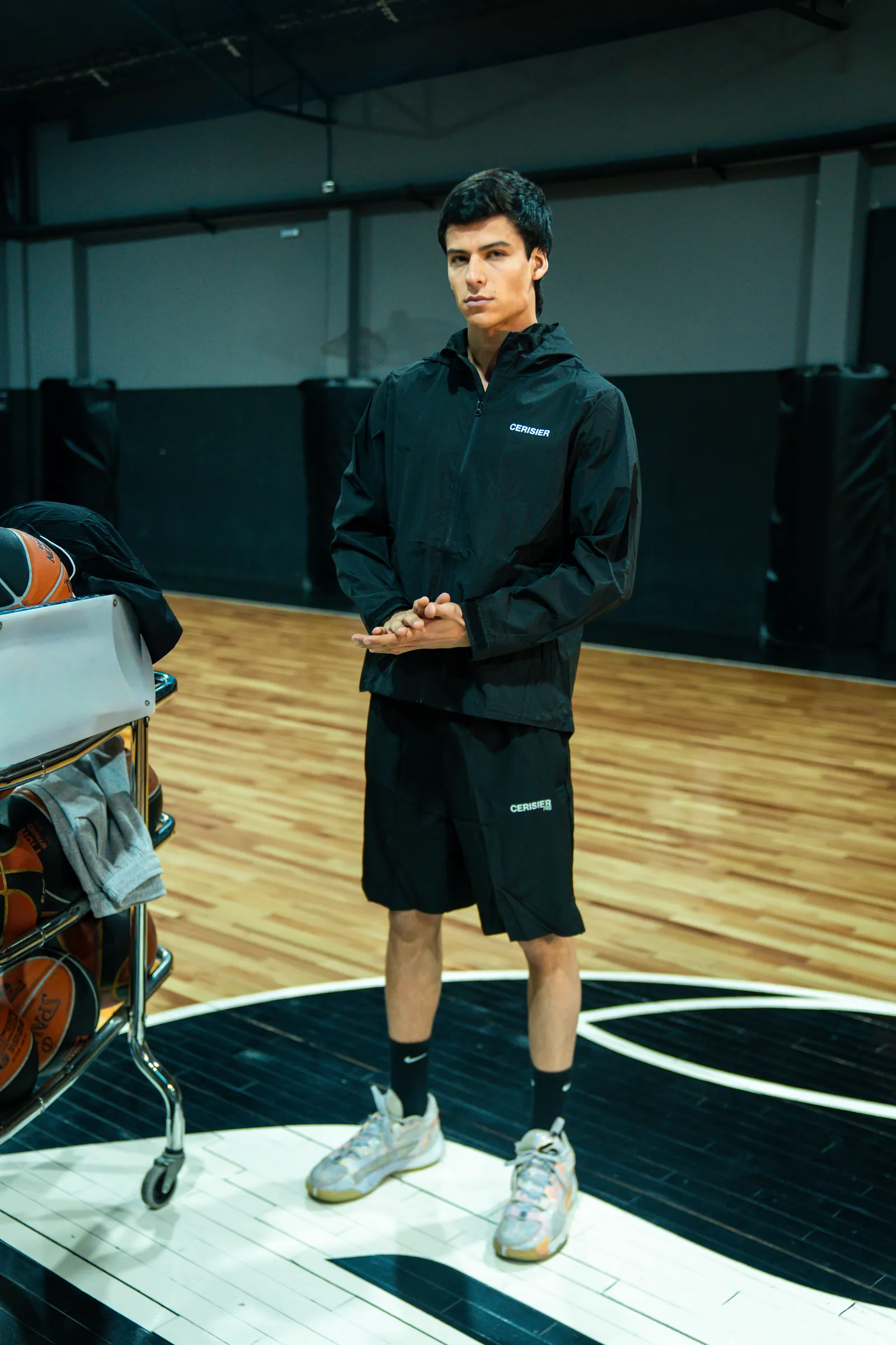 Jugador con buzo negro con capucha y short negro, de pie en una cancha