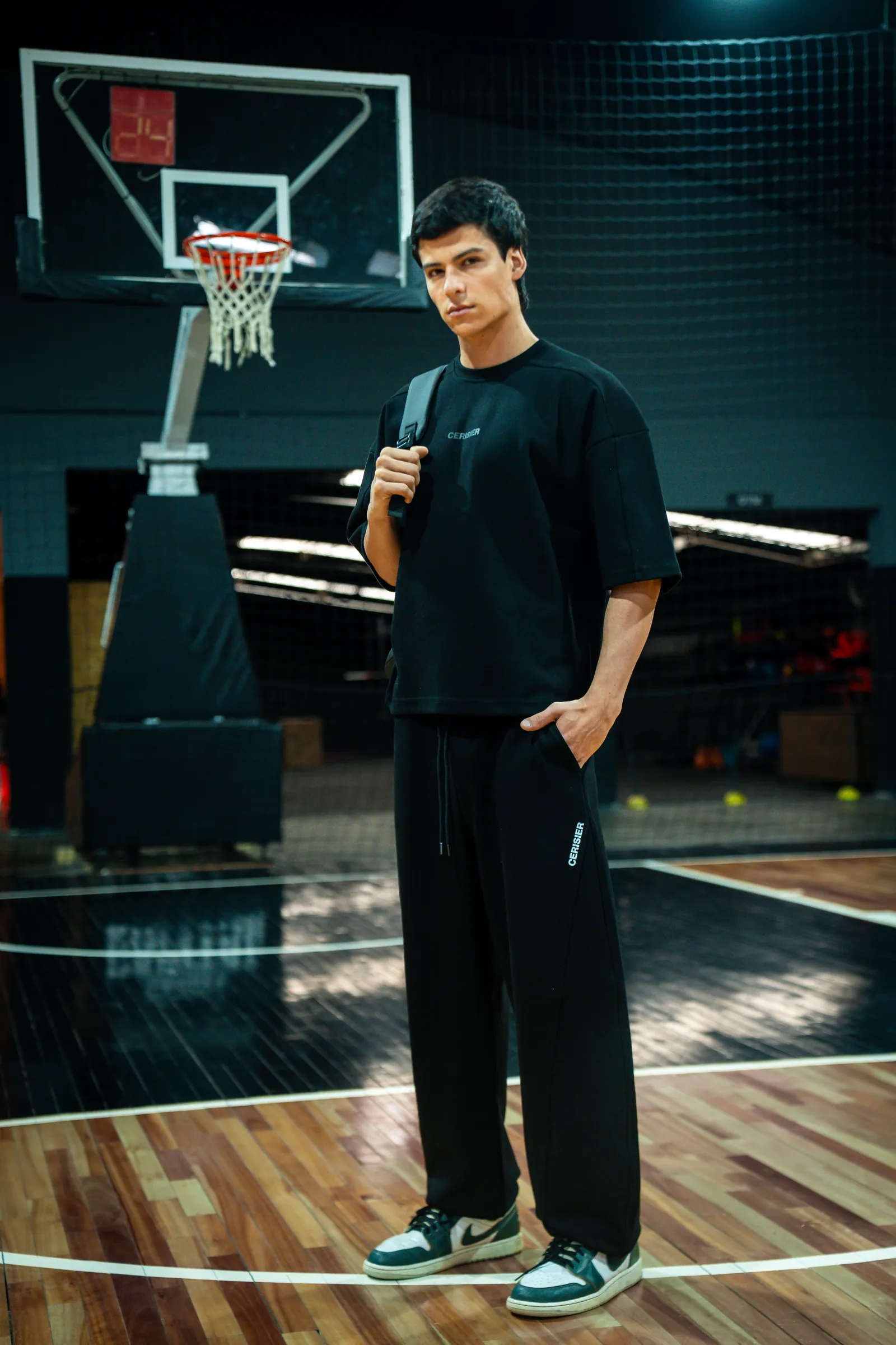 Persona de pie en una cancha, con remera negra y jogging gris oscuro