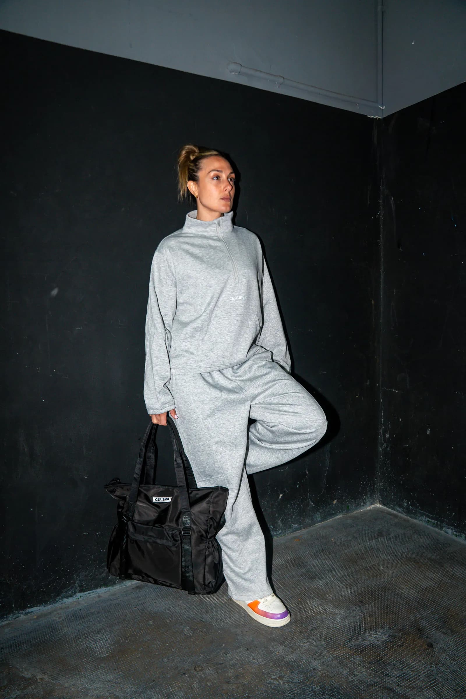 Persona con buzo gris de cuello alto y pantalón, junto a un bolso negro