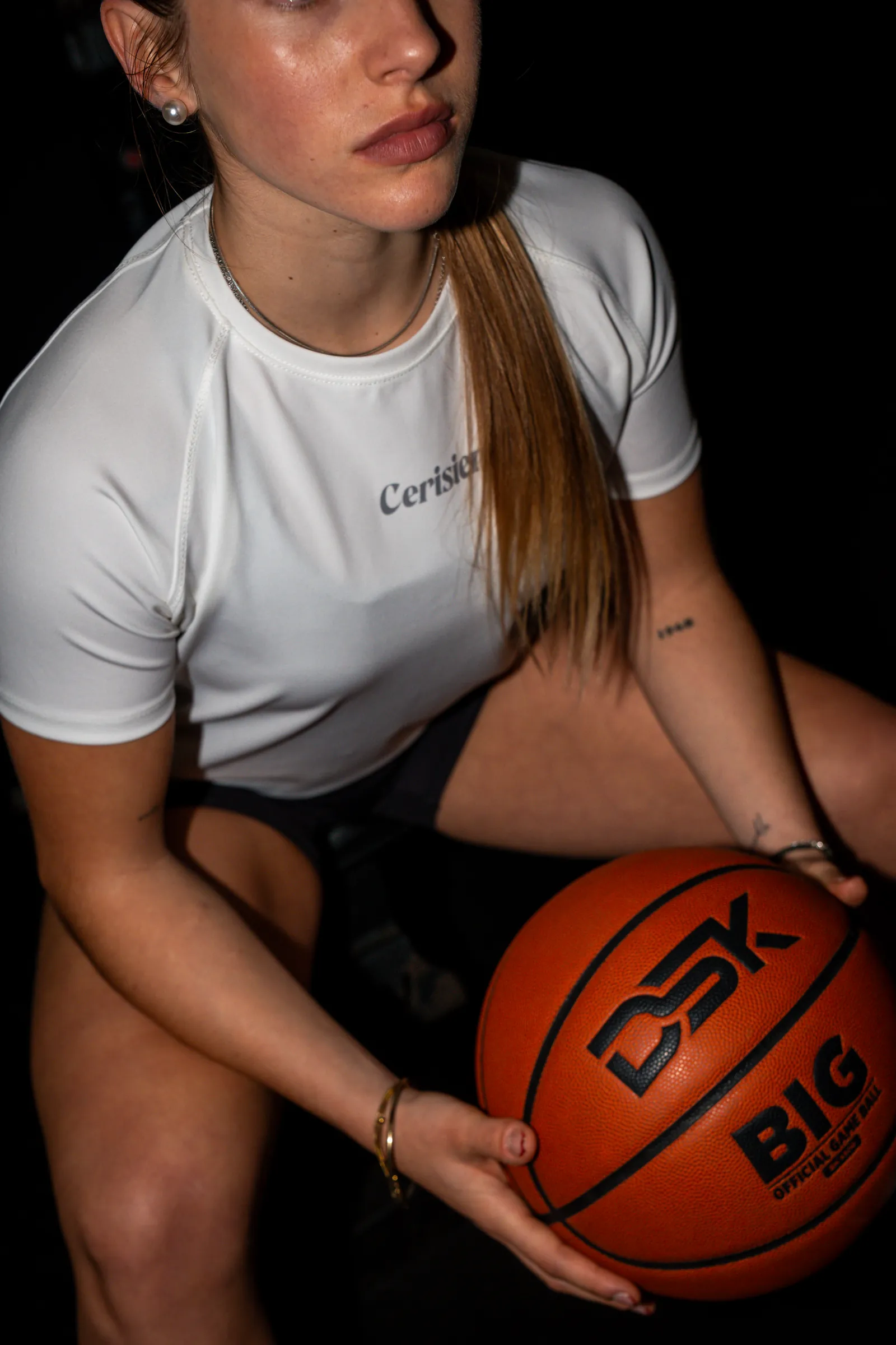 Jugadora con remera blanca sosteniendo una pelota de básquet, en primer plano